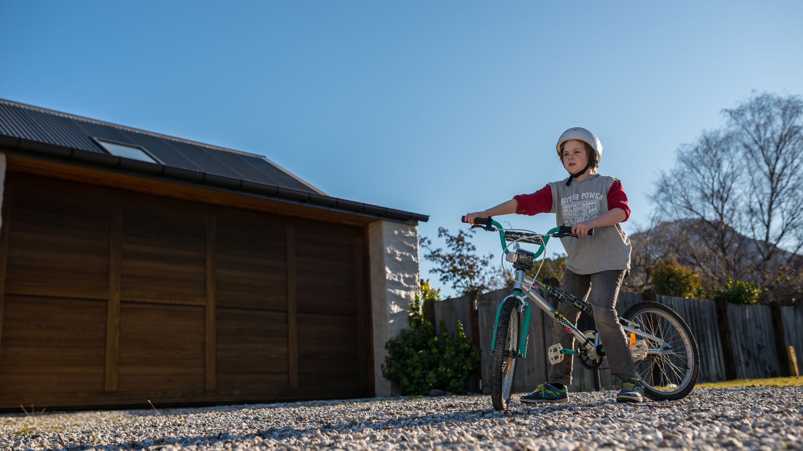 Boy riding a bike on a stable gravel driveway outside a timber garage
